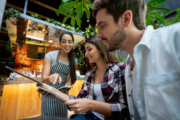 istock Beautiful waitress suggesting something from menu to customer couple looking at menu smiling 1073455472