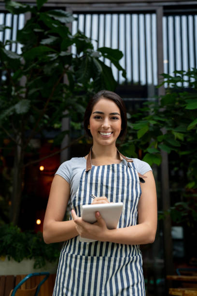 istock Portrait of latin american pretty waitress facing camera smiling while holding a notepad 1073455588
