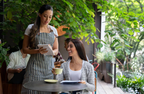 istock Beautiful cheerful female customer ordering something from menu while enjoying a coffee and waitress taking the order 1073455798
