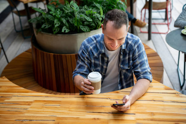 istock Handsome cheerful latin american man chatting on smartphone laughing while enjoying a take out coffee at a coffee shop 1073456754