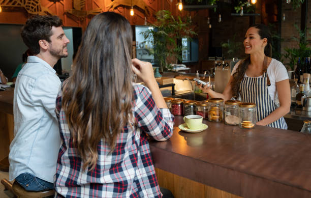 istock Friendly cheerful waitress holding an electronic card reader and male customer ready to pay at the bar counter of a restaurant 1073456944