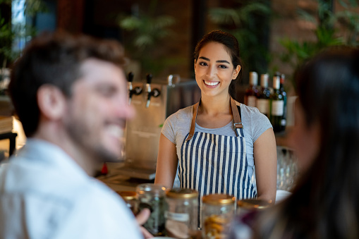 Latin american friendly waitress serving custmer couple on bar counter smiling very happy