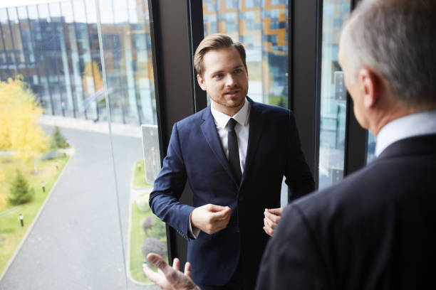 istock Content confident handsome young businessman in formal suit gesturing hands and talking to colleague while proving his point to him in office 1073477382