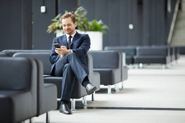 istock Smiling content young bearded businessman in formal suit sitting on leather sofa and texting sms on smartphone while waiting for business partner in lobby 1073478164