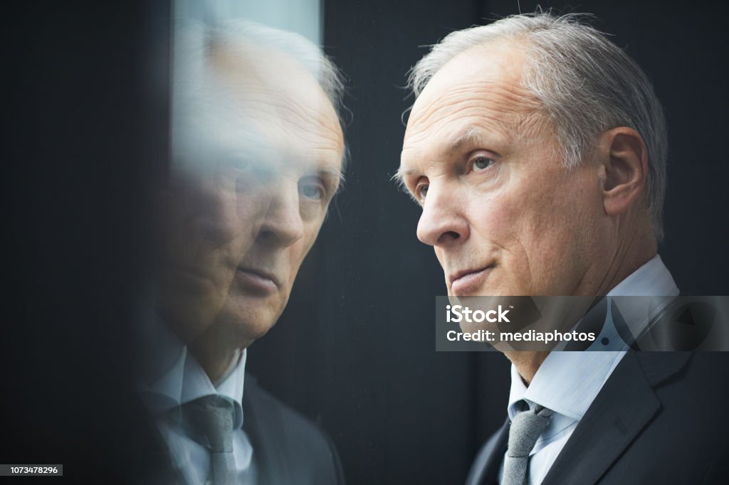 Close-up of serious pensive gray-haired mature politician with wrinkled forehead looking out window, reflection effect Pensive mature politician looking out window Politician Stock Photo