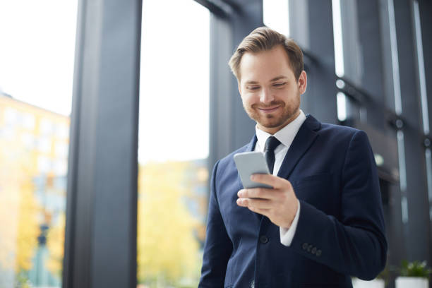 istock Smiling content handsome young businessman with beard walking over business center and using smartphone on move while reading internet news 1073486748