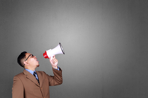 Young Asian businessman wearing shouting with megaphone, angry expression. Close up body portrait, side view