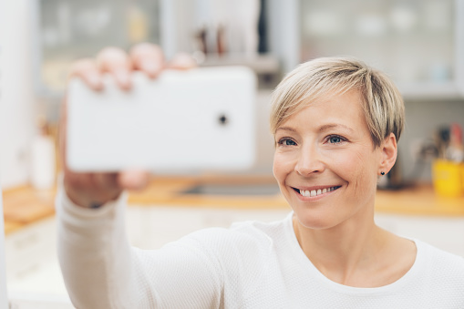 Attractive woman posing for a selfie on her mobile smiling happily as she holds the phone on high with focus to her face
