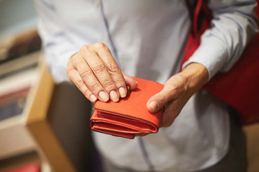 A close-up of a senior unrecognizable woman's hands holding a small red wallet.