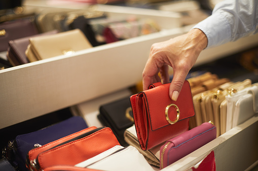 A close-up of a small red wallet being picked up from a rack in a bags and wallets store.