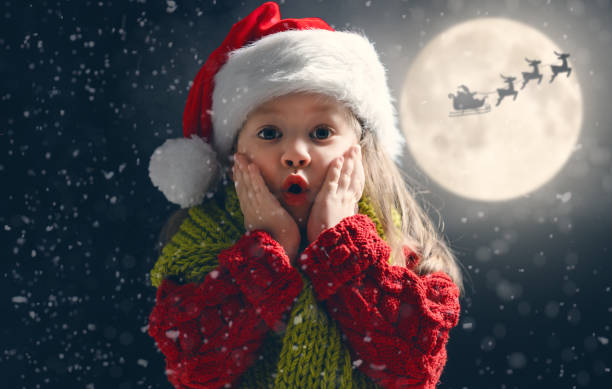 girl on snowy background Cute little child on Christmas. Santa Claus flying in his sleigh against moon sky. Happy kid enjoy the holiday. Portrait of girl with gifts on dark background. animal sleigh photos stock pictures, royalty-free photos & images