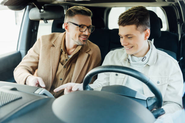 uśmiechnięty przystojny ojciec uczy nastoletniego syna prowadzącego samochód - learning to drive zdjęcia i obrazy z banku zdjęć