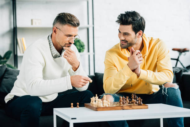 istock handsome son and mature father playing chess on weekend at home 1073596262