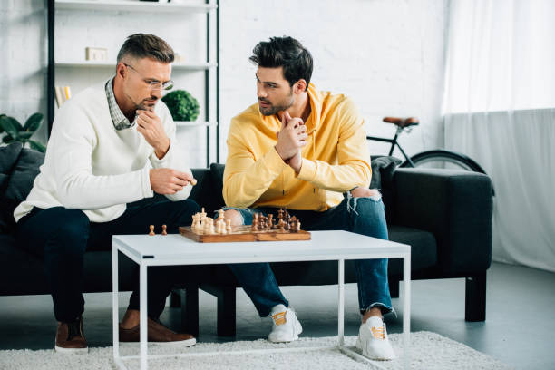 istock pensive son and mature father playing chess together on weekend at home 1073596276