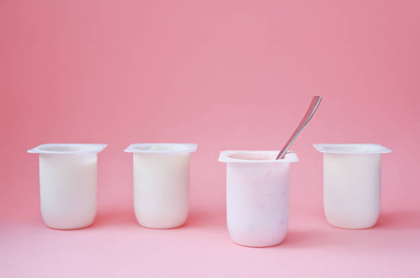 quattro yogurt in tazze di plastica bianca. stile minimale. concetto di scelta migliore. - yogurt yogurt container strawberry spoon foto e immagini stock