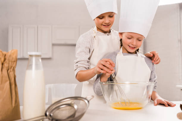 istock boy with sister in chef hats whisking eggs in bowl at table in kitchen 1073605202