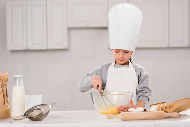 istock concentrated kid in chef hat whisking eggs in bowl at table in kitchen 1073605226