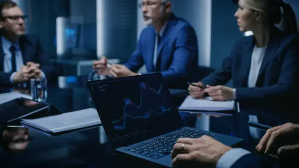 Photo of On the Table Laptop Showing Statistics: Team of Politicians, Corporate Business Leaders and Lawyers Sitting at the Negotiations Table in the Conference Room, Trying to Come to an Agreement.