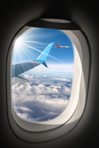 Two commercial airplanes (aircraft wing and plane) photographed through the porthole window, while flying above the clouds.