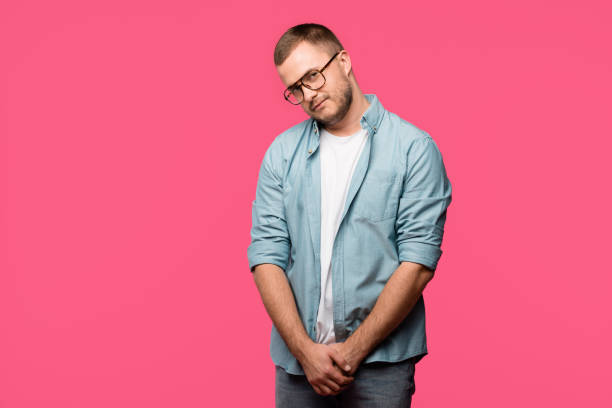 istock shy young man in eyeglasses looking at camera isolated on pink 1073620198