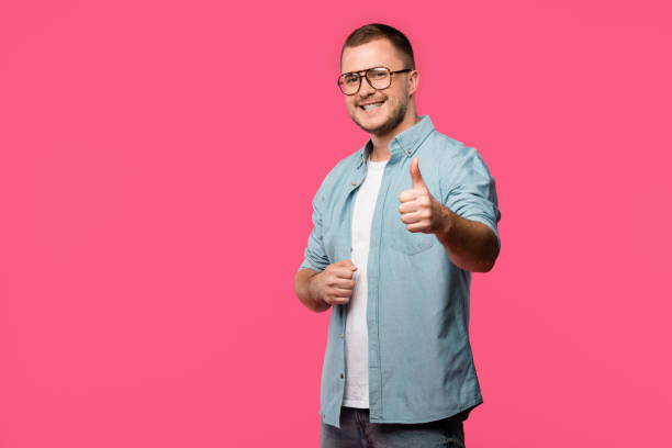 istock handsome young man showing thumb up and smiling at camera isolated on pink 1073620208