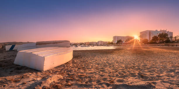 Sand shore with pastel sky, waves and sunbeams on stone during sunset Ibiza, Spain