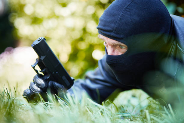 un homme masqué avec arme à feu est à l’affût pour quelqu'un - gun men spy suit photos et images de collection