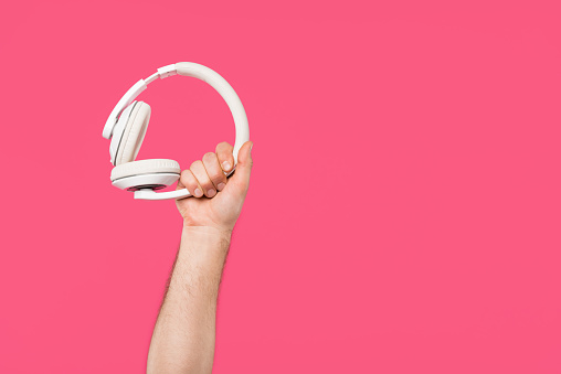 cropped shot of man holding white headphones isolated on pink