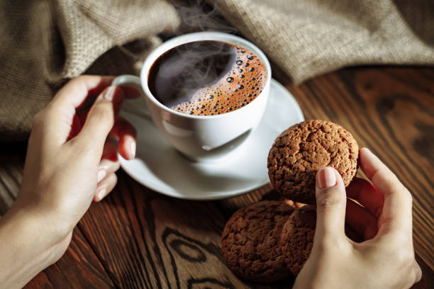 istock Hands holding cookie and coffee on wooden table 1073636352