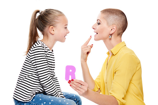 Cute young girl with speech therapist practicing correct pronunciation. Child speech therapy concept on white background. Speech impediment corrective exercises.