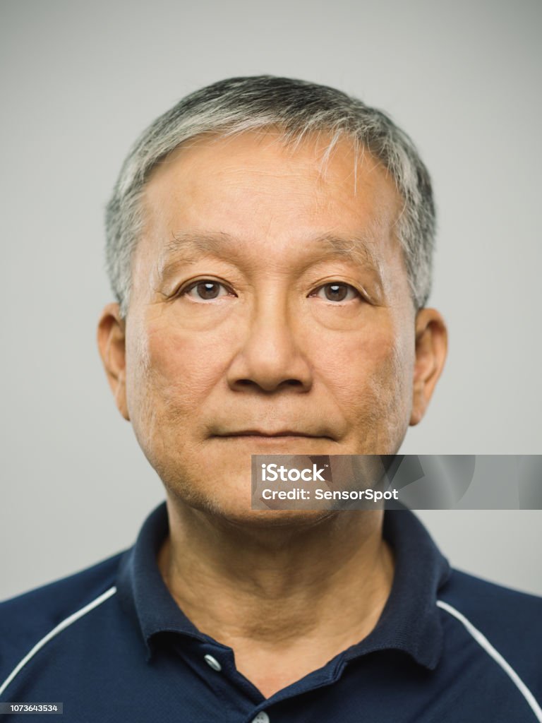 Real chinese senior man with blank expression Close up portrait of senior asian man with blank expression against gray background. Vertical shot of real chinese man staring in studio with gray hair. Photography from a DSLR camera. Sharp focus on eyes. Portrait Stock Photo