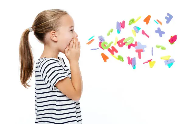 Photo of Cute little girl in stripped T-shirt shouting out alphabet letters. Speech therapy concept over white background.