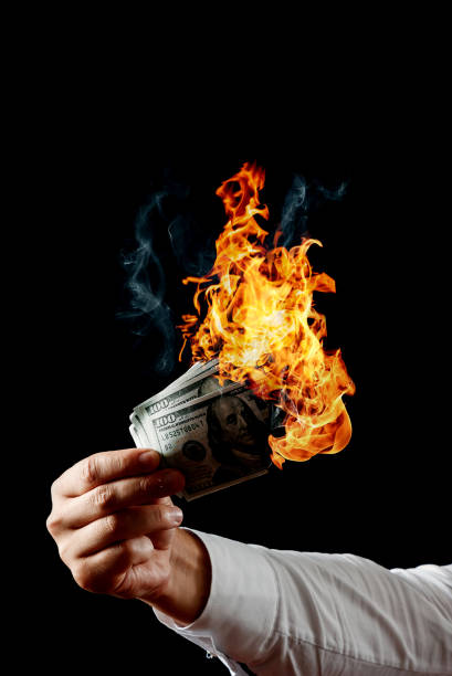 istock Male hand close-up, holds burning money in hands, burning US dollars. Black background, isolate. The concept of inflation, a decrease in the purchase of foreign currency, and devolution. 1073648480