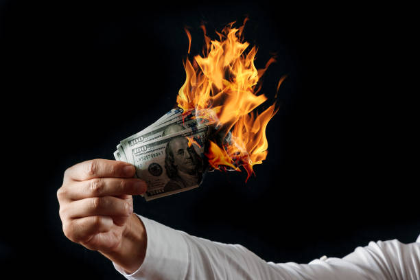 istock Male hand close-up, holds burning money in hands, burning US dollars. Black background, isolate. The concept of inflation, a decrease in the purchase of foreign currency, and devolution. 1073648496