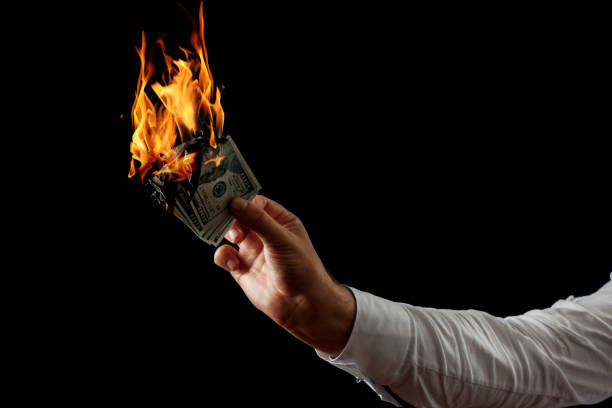 istock Male hand close-up, holds burning money in hands, burning US dollars. Black background, isolate. The concept of inflation, a decrease in the purchase of foreign currency, and devolution. 1073648504
