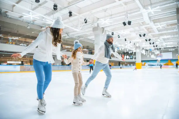 Photo of smiling family holding hands while skating together on ice rink