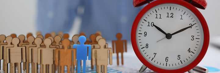 Businessman with his hand puts a miniature silhouette of a man in his rightful place. Red alarm clockwork means a staff schedule for each unit of the work cycle of an enterprise