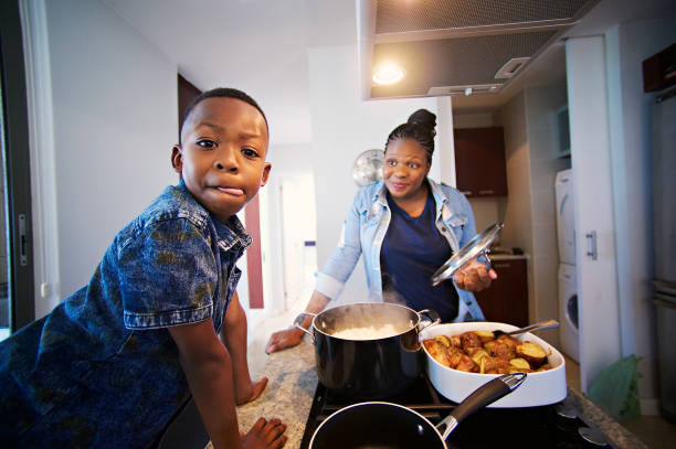 That looks scrumptious; Boy Licking lips African mother and son busy at in the kitchen with the boy looking at the camera licking his lips while the other smile Strand Cape Town South Africa south african braai stock pictures, royalty-free photos & images