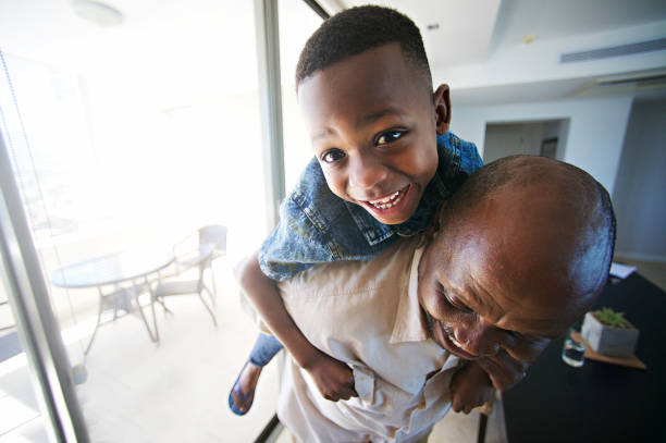 istock Grandfather playing having fun with son on his back indoors looking at camera 1073672864