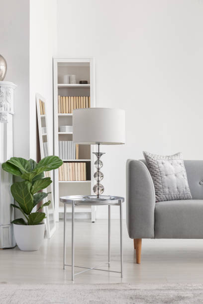 istock Elegant white lamp on small silver table next to grey sofa in spacious new york's style living room 1073680328