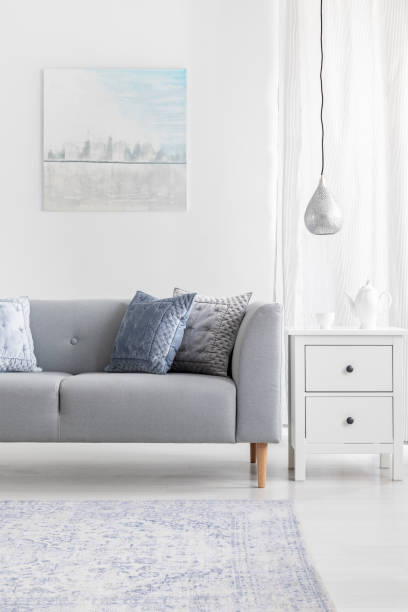 Vertical view of rustic carpet in elegant living room interior with grey sofa, white commode and silver lamp, real photo with mockup on the wall
