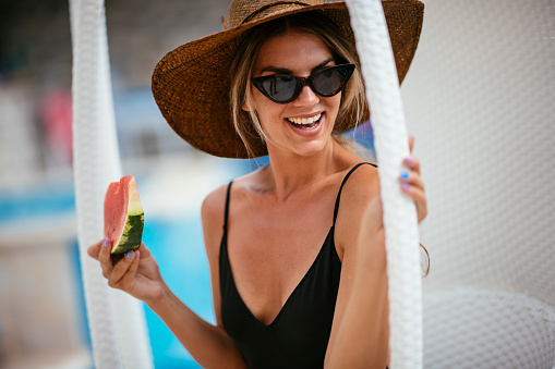 Woman enjoying slice of watermelon at swimming pool. Shadow DOF. Developed from RAW; retouched with special care and attention; Small amount of grain added for best final impression. 16 bit Adobe RGB color profile.
