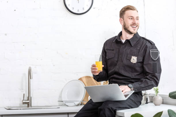 istock handsome man in police uniform sitting on kitchen table, drinking orange juice and using laptop 1073686218