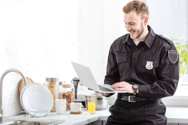 istock smiling police officer standing and using laptop at kitchen 1073686228