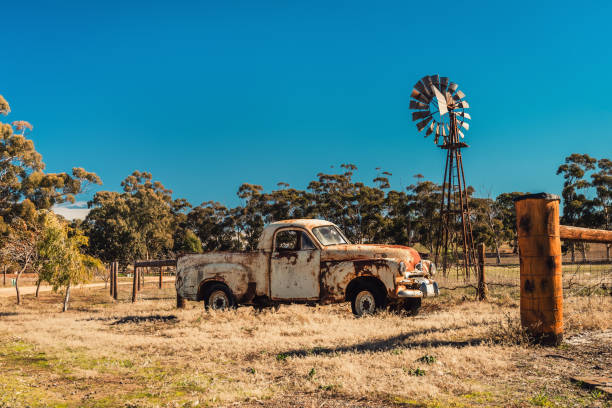 Kapunda, South Australia - June 17, 2017: Rusty Holden FJ Ute and vintage Kookaroo windmill on display near farm entrance from highway