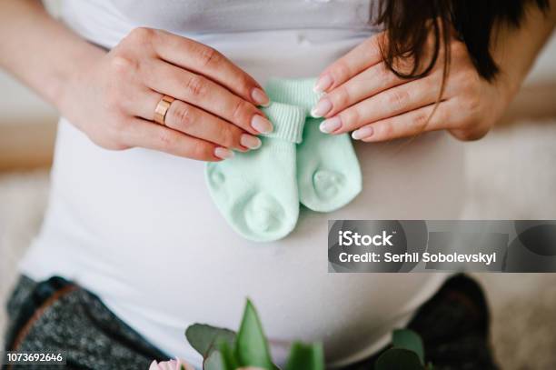 Cropped Image Pregnant Woman Holding Socks For A Baby On Her Belly Stomach Pregnant Hugging Tummy At Home Motherhood Concept Baby Shower Stock Photo - Download Image Now