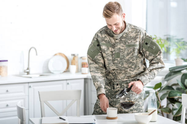 istock Man in camouflage uniform pouring coffee in cup at kitchen 1073700036