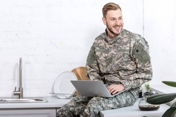 istock smiling soldier in military uniform sitting at kitchen countertop and using laptop 1073700130