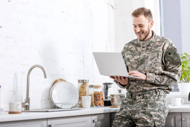 istock handsome army soldier in uniform using laptop at kitchen 1073700132