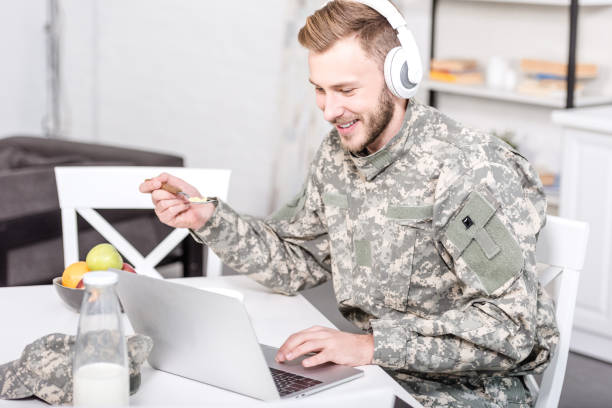 istock smiling soldier in headphones using laptop at kitchen table while having breakfast 1073700208
